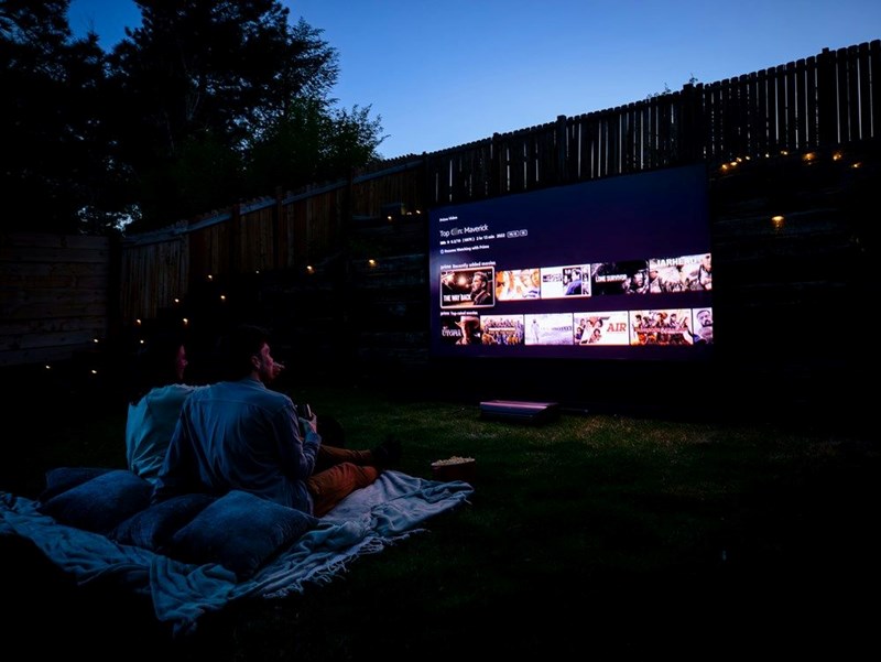 People sitting on a blanket while they watch a movie being projected in the garden. Representation.