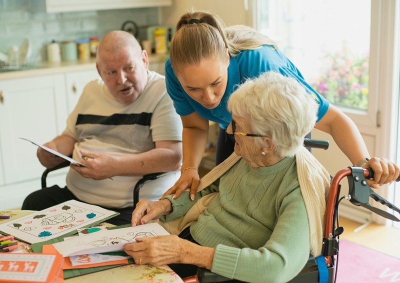 An elder caregiver helping grown adults. Representation.