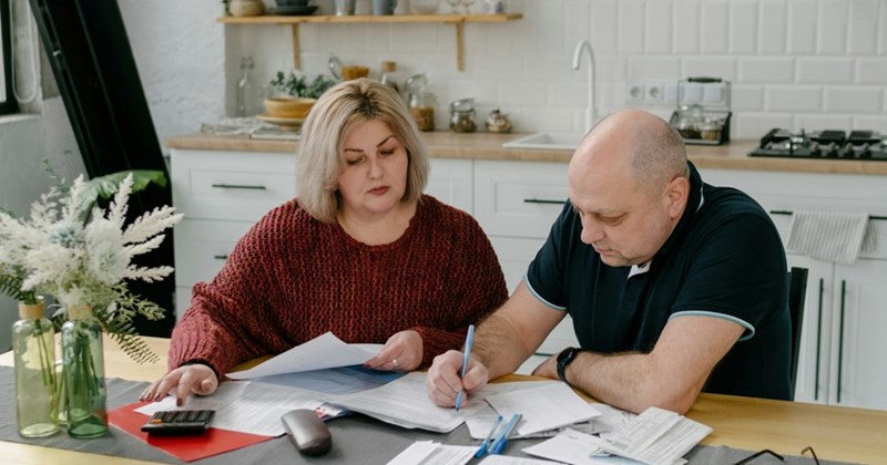 A middle-aged couple organize bills while sitting at a kitchen table