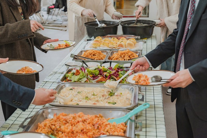 Employees gathered around a potluck buffet, representing coworkers sharing homemade food at an office going-away celebration.