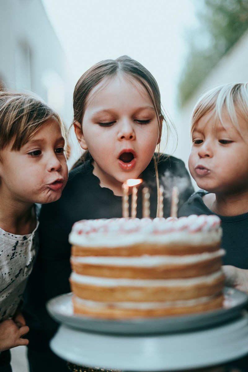 Children blowing out birthday candles together, illustrating a girl celebrating her special day with visiting cousins from overseas.
