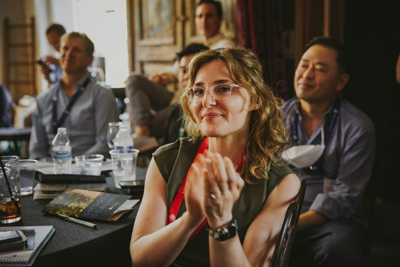 A group of employees sit around a conference room at lunch clapping for a presentation
