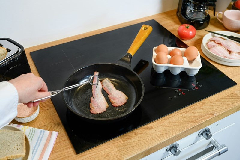 A person fries bacon in a pan on a stovetop