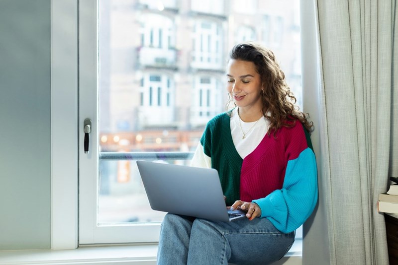 A woman sitting at the window, working on her computer. Representation.