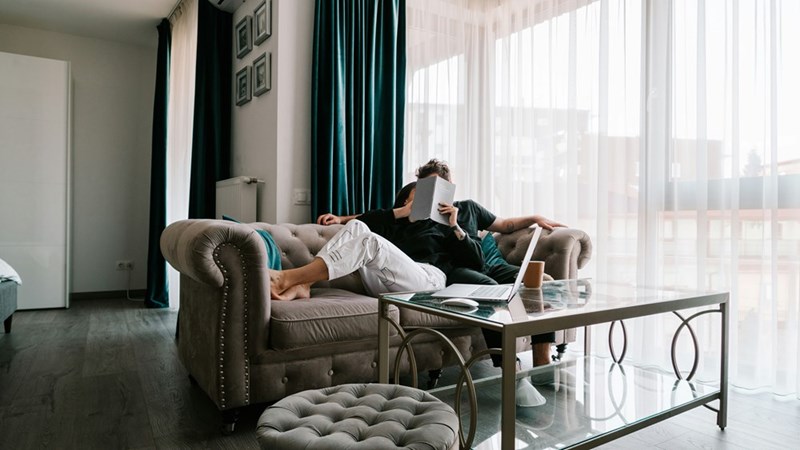 A person resting on a sofa while he reads a book. Representation.