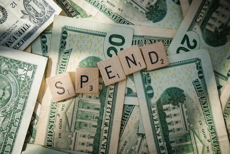 Money on a table with wooden letters spelling ‘spend’.
