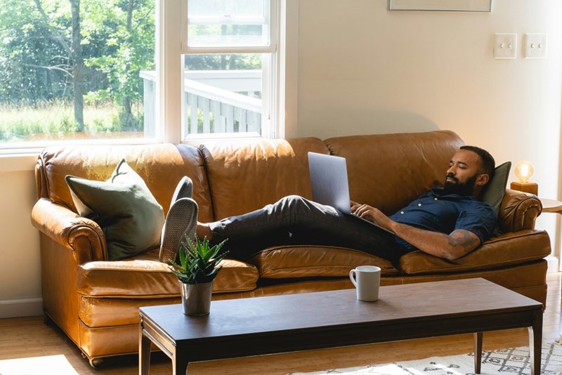 Man relaxing on a couch while he catches up on his emails.