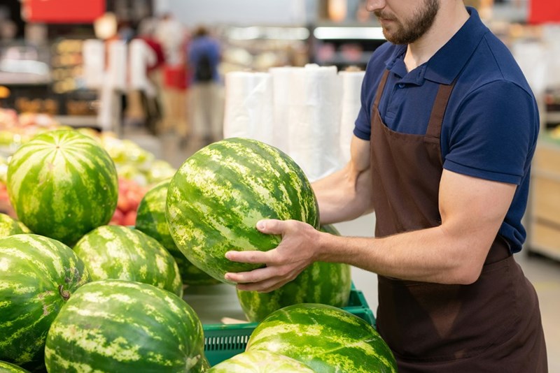Grocery store employee stocking and handling fresh produce.