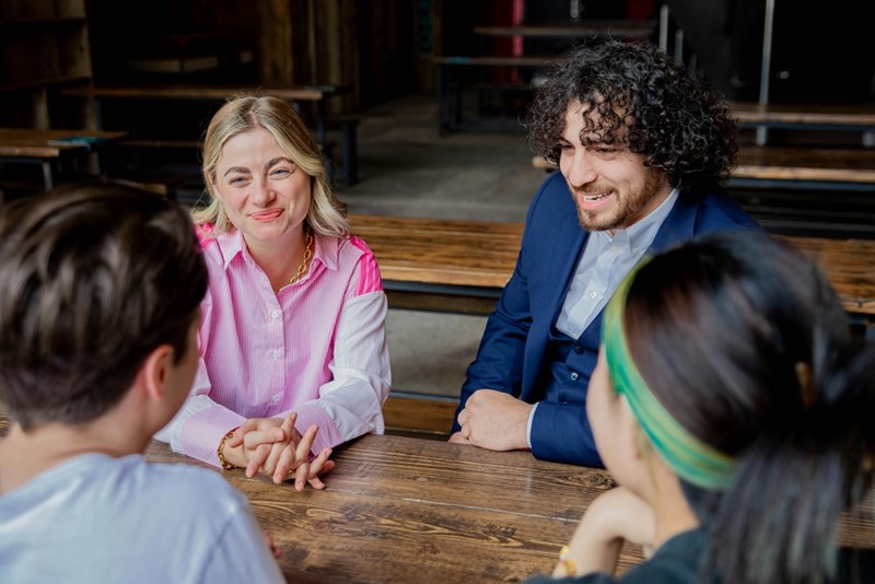 A couple sits at the edge of a table across from the girlfriend's parents