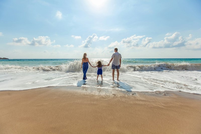 A family of three holding hands on the seashore. Representation.
