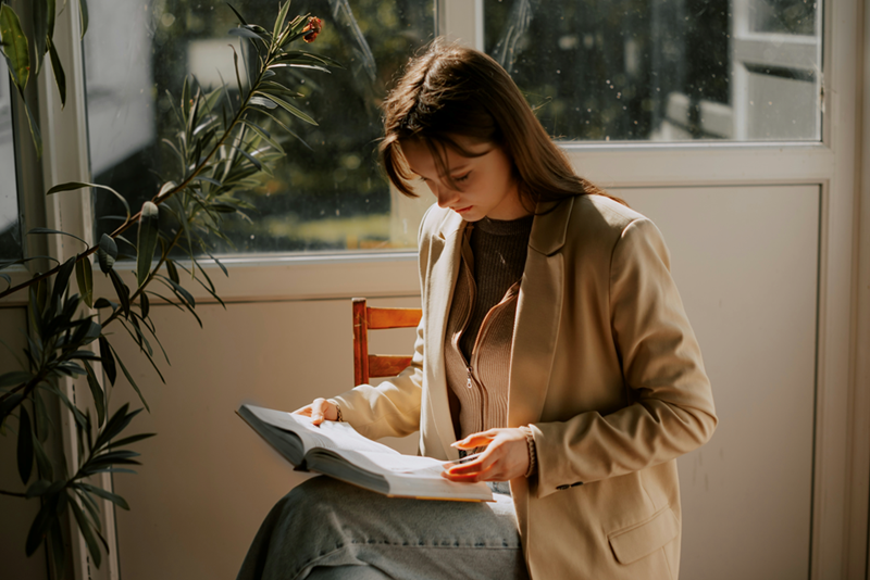 A woman looks at a book in her lap, confused