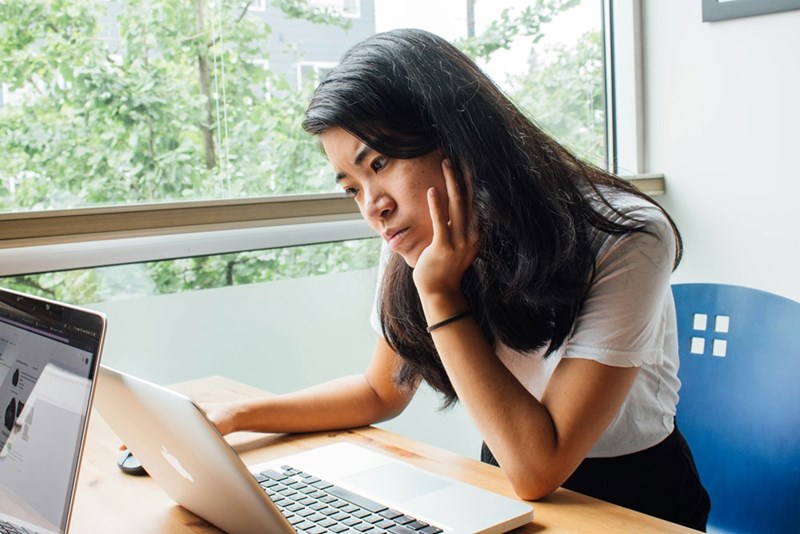 A woman looks down at her computer, confused