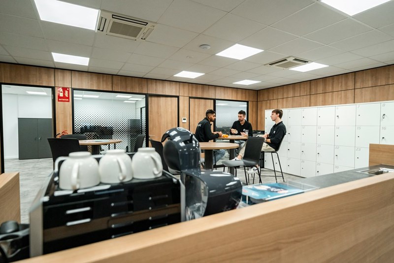Coworkers talking inside an employee break room surrounded by workplace lockers.