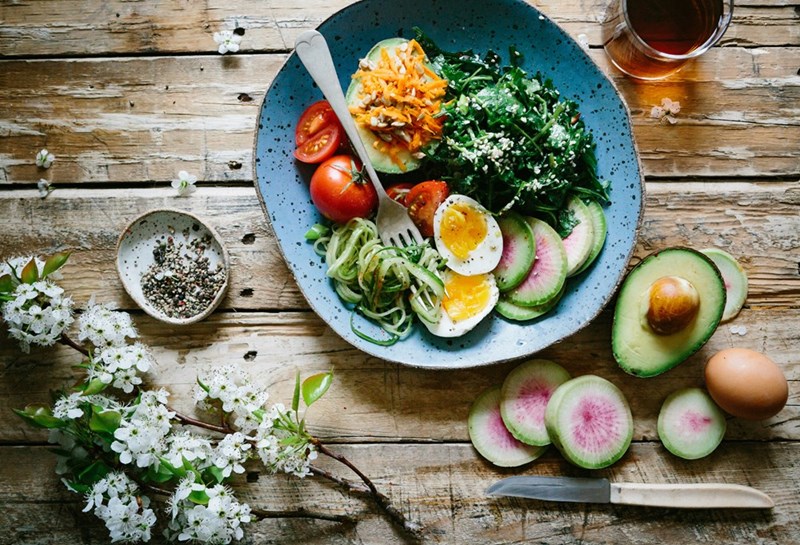 A salad with egg, tomato, avocado, greens, and seeds.