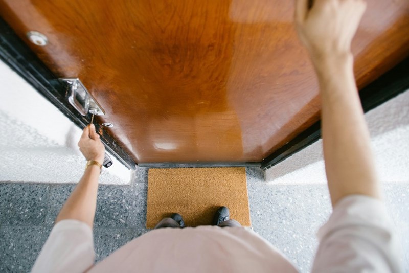 Person unlocking and opening an apartment door with a key from the outside.