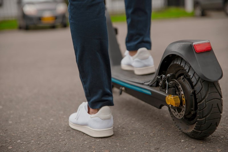 Person standing next to a scooter, an available alternative to using a borrowed family car.