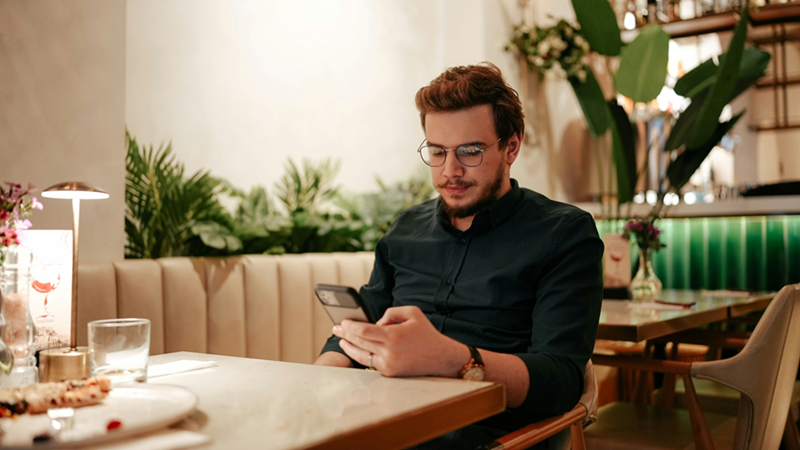 A diner sits at a table in a restaurant, looking at his phone