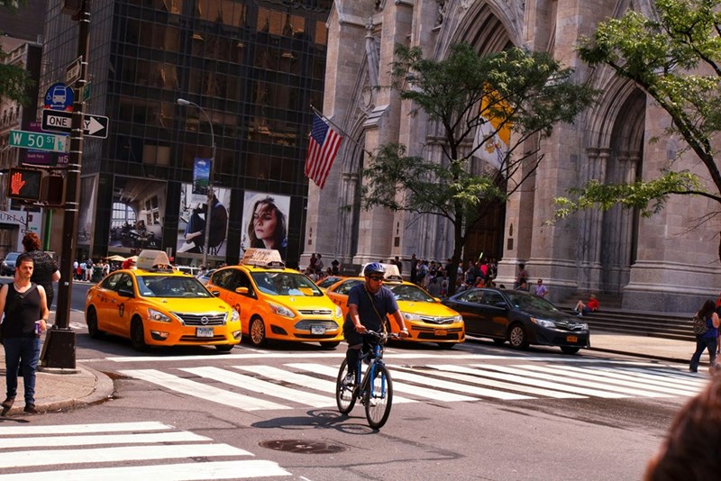 Cyclist rides through New York City streets, representing the employee's new required commute between the main office and the company's field location.