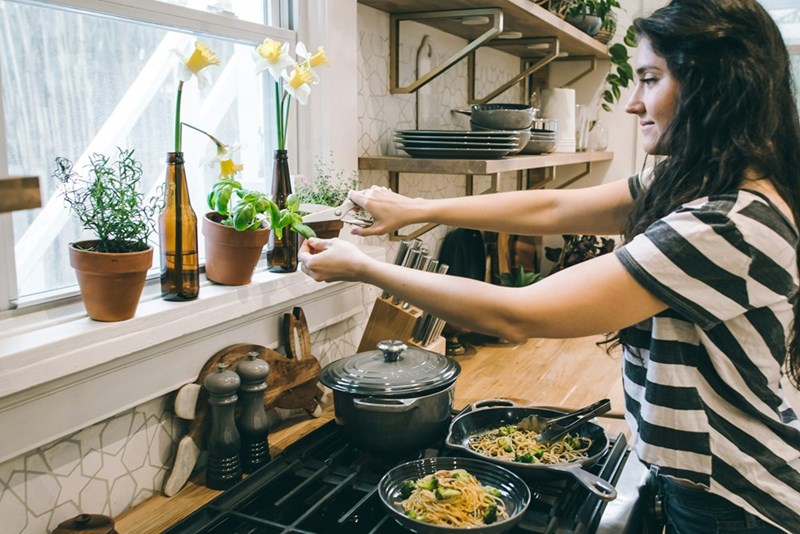 Young woman spends time in a shared apartment kitchen wearing a personal item from the other girl.