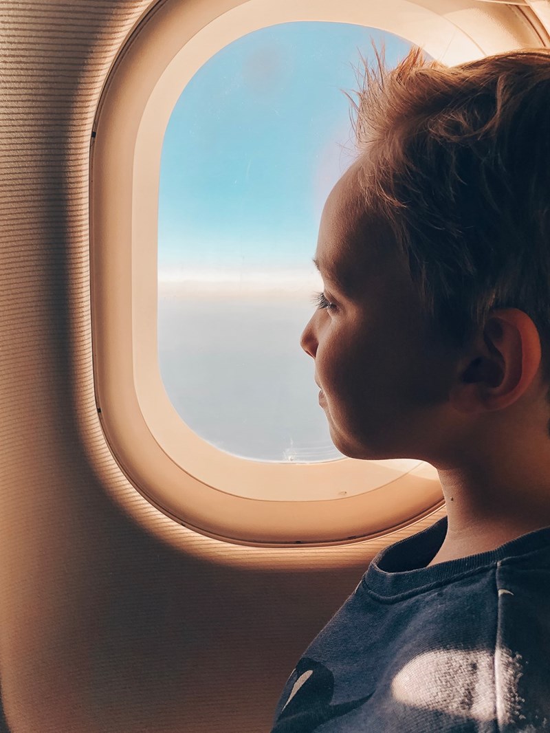 Young boy sits by an airplane window, looking out at the sky.