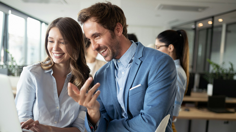 A representation of a male and female coworker looking at something together on a laptop