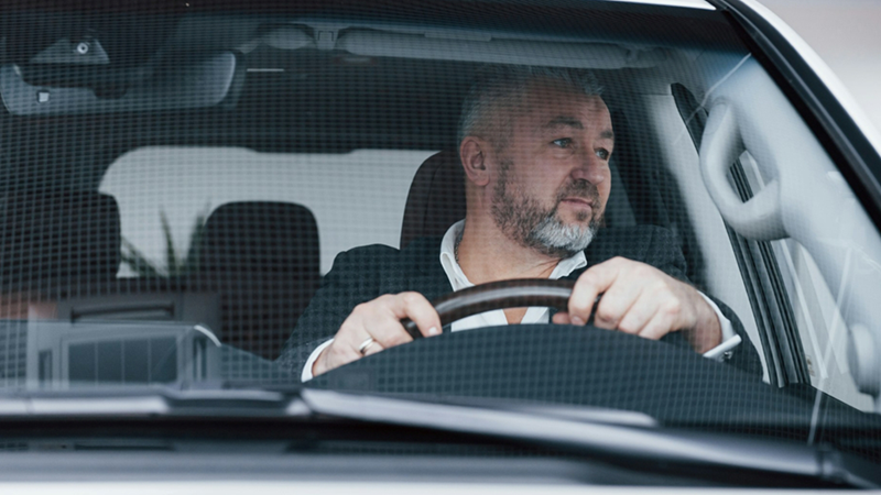 A middle-aged man looking out his side window while driving a car