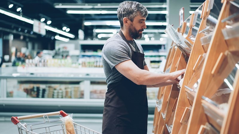 A supermarket worker organizes products on store shelves during a shift.