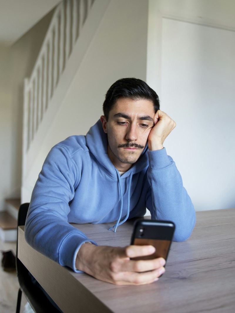 A frustrated person stares at their phone after receiving an unexpected message from their ex about their friend's wedding.