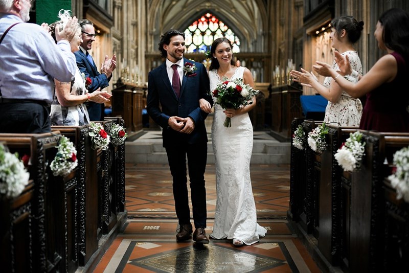 A happy couple walks down the aisle at a wedding while guests celebrate around them.