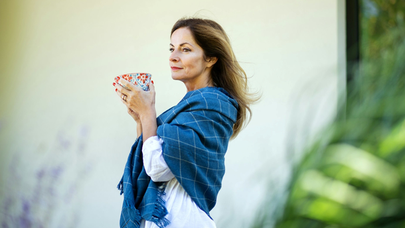 A representation of a woman wearing a shawl, holding a large teacup with two hands while standing outside