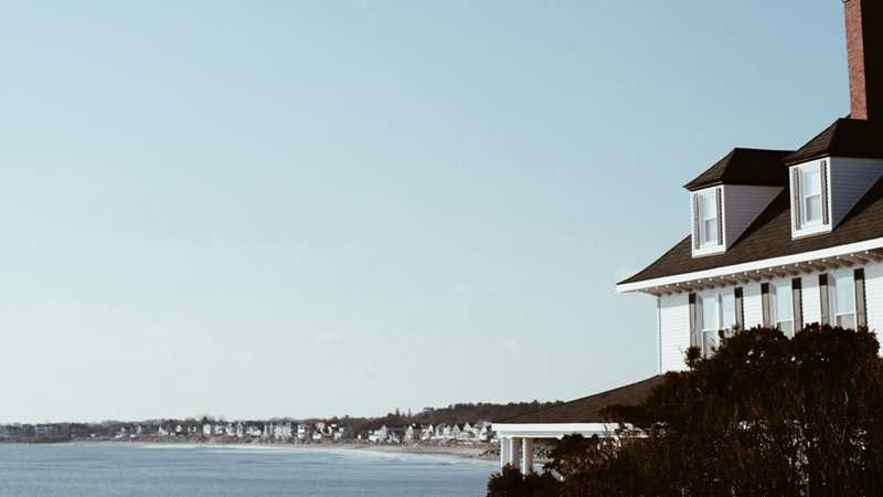 The outside of a white vacation home on a clear day by a body of water