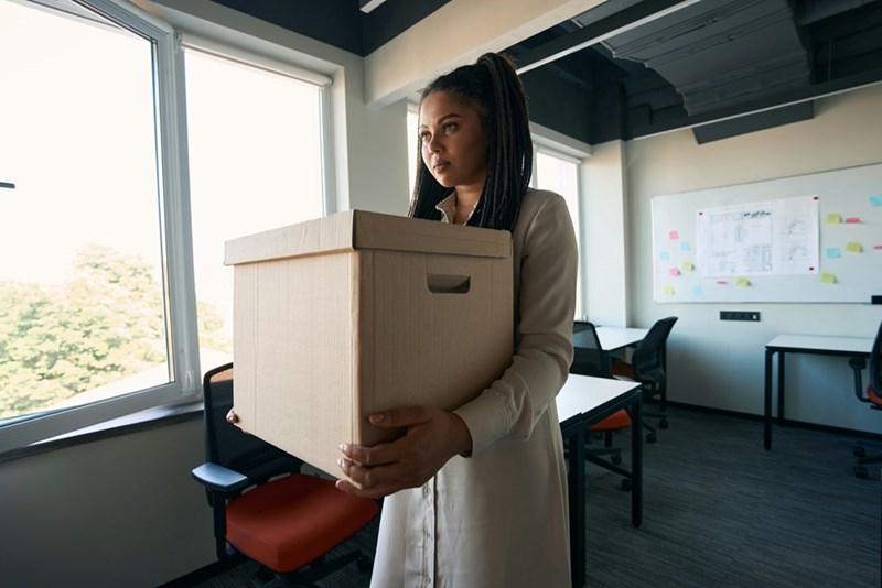 A businessperson carries their belongings out of the office after being fired