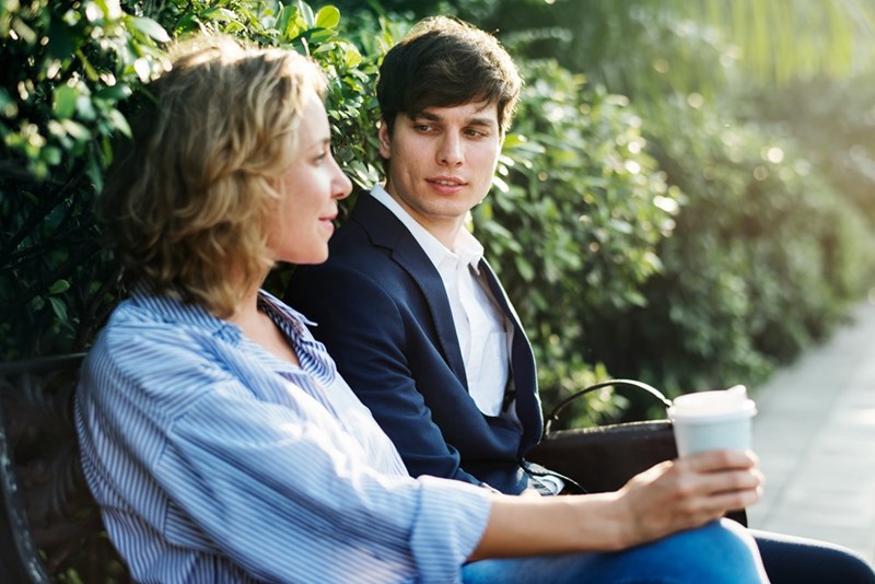 Two people sit next to each other on a bench drinking coffee