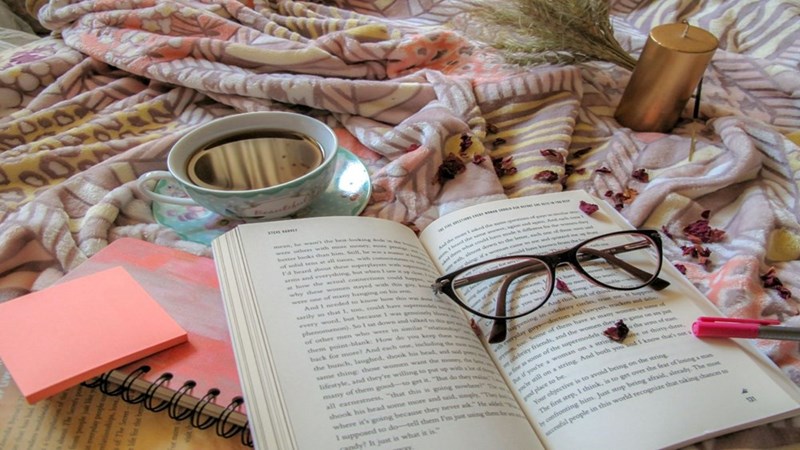 A book, a cup of tea, and a notebook in a bed.