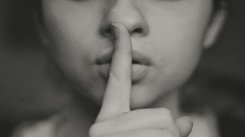 A person with a finger across their mouth indicating silence. Representation.