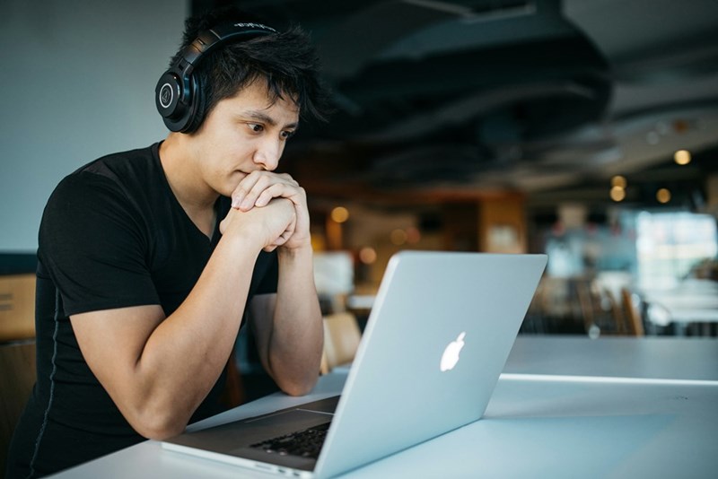 A man looking at his computer with headphones on. Representation.