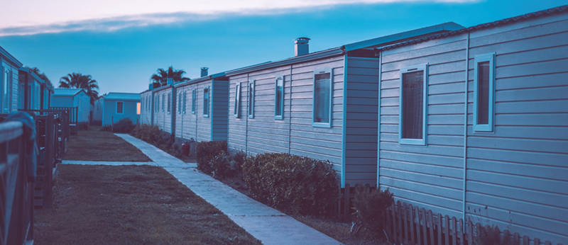 A row of trailer park trailers seen under an ambient setting sun.