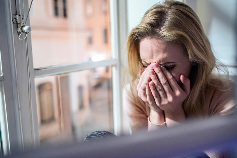 A woman appears overwhelmed and emotional while sitting alone.