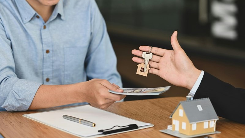 A real estate transaction is represented by one person exchanging money while another hands over a set of house keys.