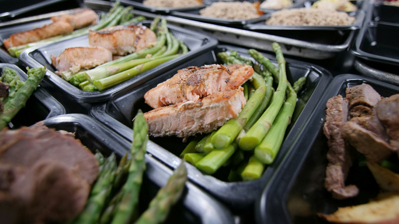 Close-up of multiple black plastic trays filled with meat and vegetables