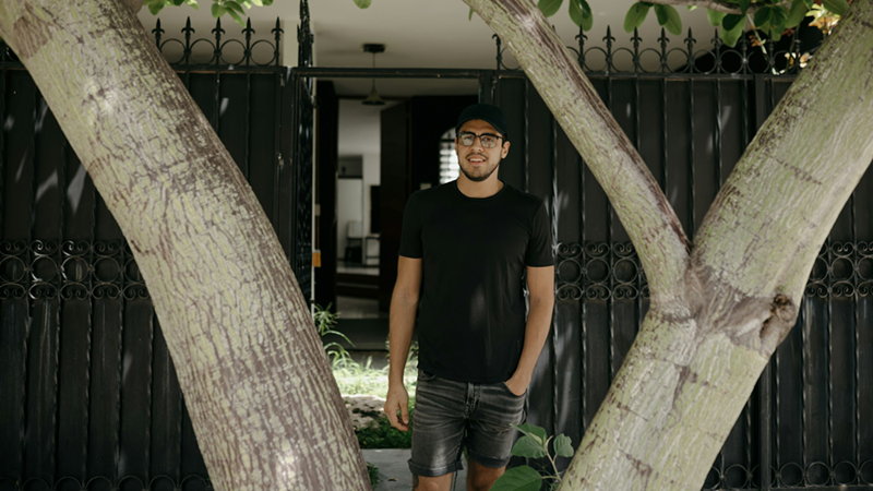 A man standing in front of a tall black gate and behind a split tree trunk