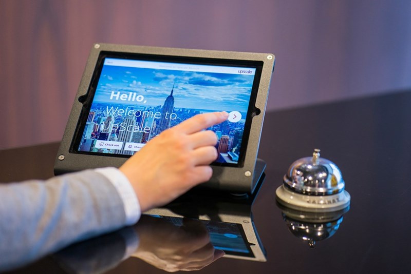 A person working with a tablet at the front desk of a hotel lobby. Representation.