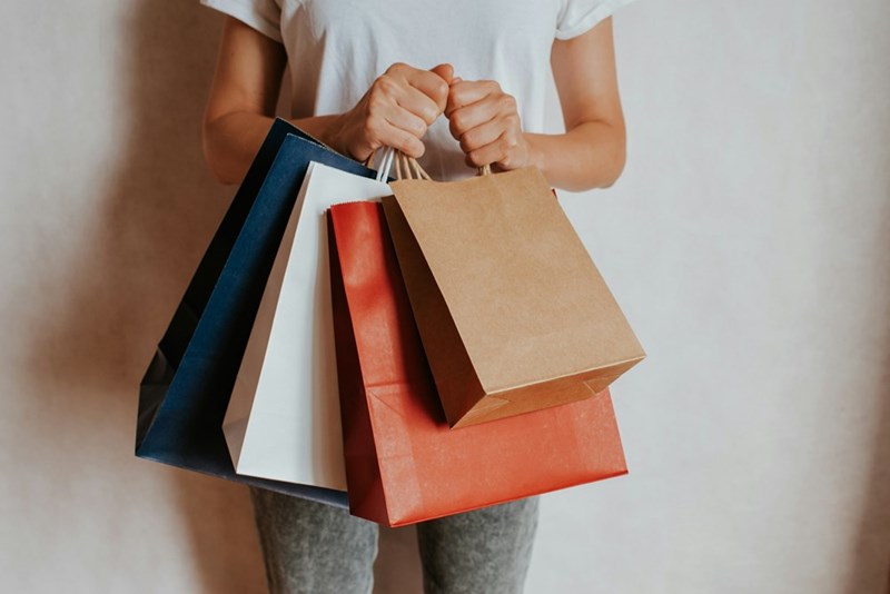 A woman stands in jeans and a t-shirt, holding several shopping bags tightly, ready to return them.