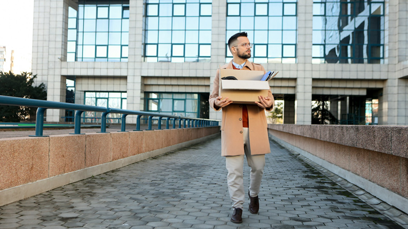 A representation of a former employee walking outside a building while holding a cardboard box of belongings