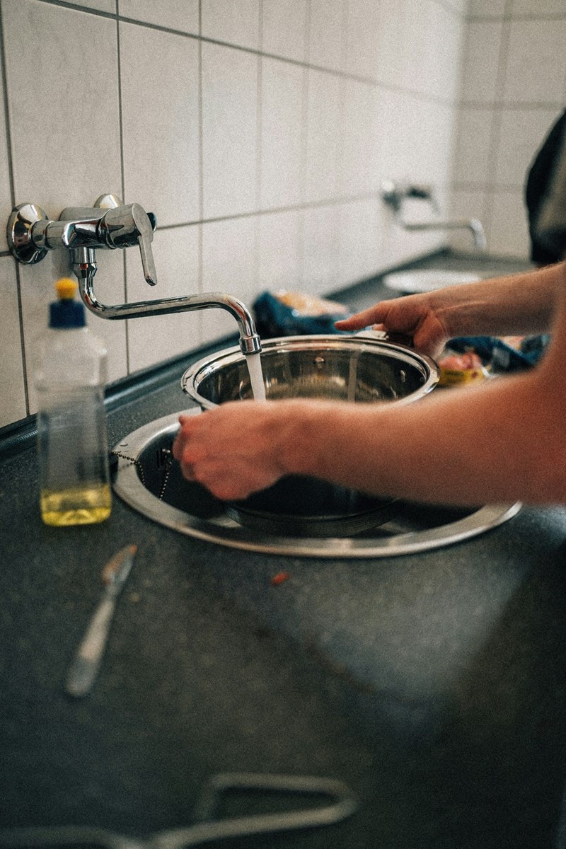 Bakery worker washing dishes during a trial shift after spending several hours cleaning and organizing items in the kitchen.