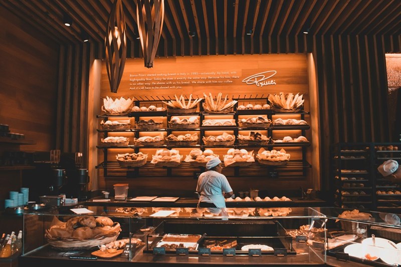 Bakery employees working behind the counter during a busy shift as a new worker learns the responsibilities of the job.