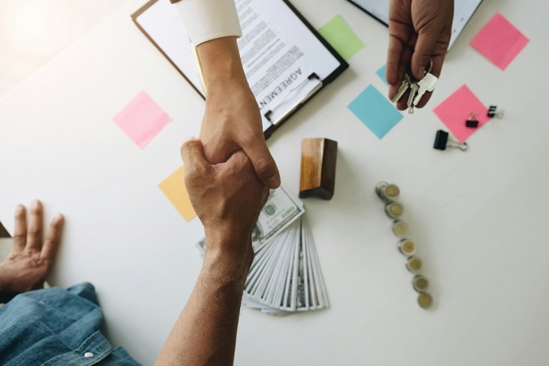Money, house keys, and an agreement sit on a table as a financial arrangement connected to buying a home is discussed.