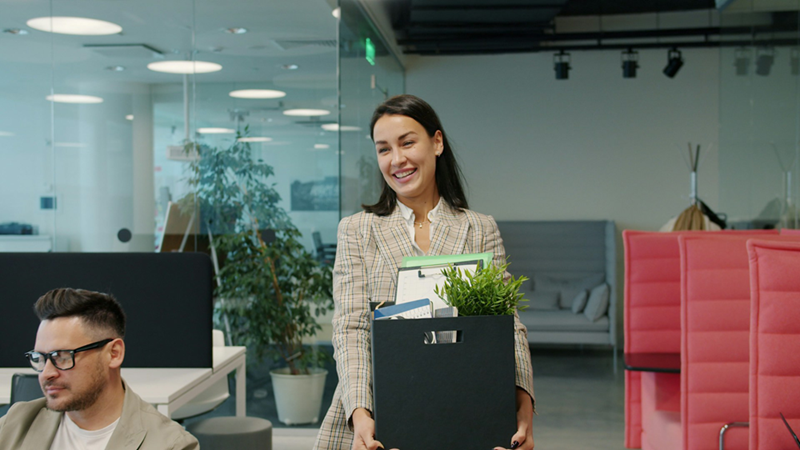 A female employee carrying a box of belongings through an office
