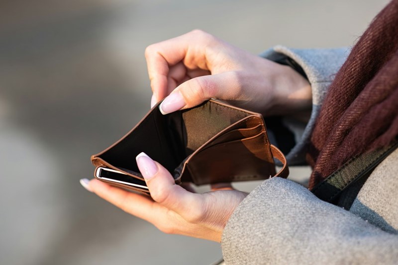 Close-up of a woman holding open an empty wallet, representing financial stress and difficulty covering everyday expenses.