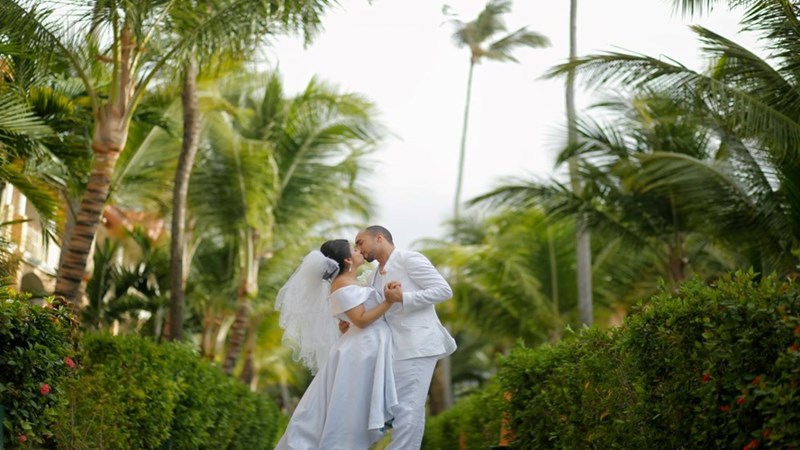 A couple getting married with palm trees surrounding them. Scene shown is a visual representation.